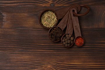 Fototapeta na wymiar Set of spices - black pepper peas, clove, hot red pepper and exotic spice at the measuring spoons. dark wood background 