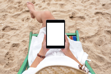 Top view mockup image of a woman holding and using a black tablet pc with blank desktop screen while laying down on a beach chair