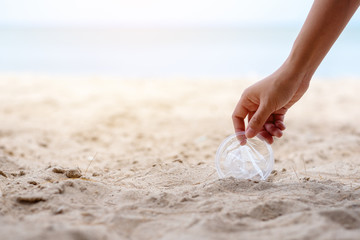 A hand cleaning and picking up a plastic glass trash on the beach