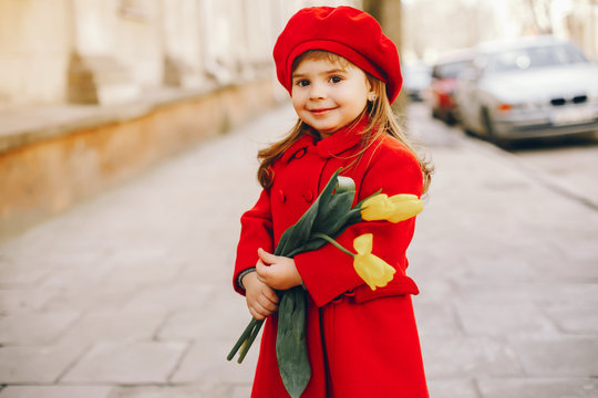 little beautiful girl in red beret and red coat walking in the autumn city with a bouquet of yellow tulips