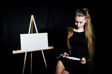 Beautiful woman artist painter with brushes and oil canvas posing in studio isolated on black.