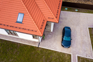 Aerial top view of house metal shingle roof with attic windows and black car on paved yard.