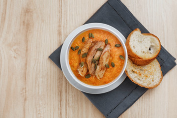 Pumpkin soup with smoked turkey and pumpkin seeds in a white plate. Two croutons near the soup.