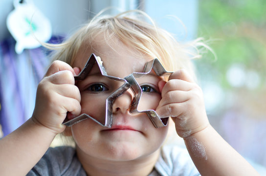 Little smiling girl holds in hands shapes of stars to baking cookies and has a fun. Christmas time.