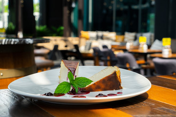 Fototapeta premium San Sebastian cheesecake slices decorated with cherry and mint leaves and blurred restaurant background