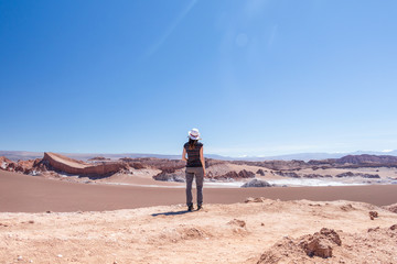 Back view of young blond casual woman in hat explore stunning landscape of Moon Valley in Atacama...
