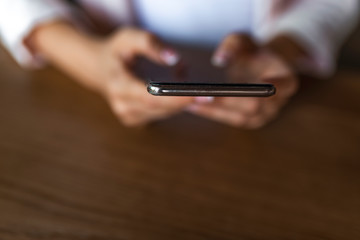 Closeup image of a woman's hands holding , using and pointing at smart phone on wooden table in vintage cafe. Woman typing text message on smart phone in a cafe. Hands holding phone