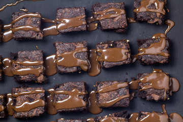 Chocolate brownie squares dribbled with ganache on black textured background