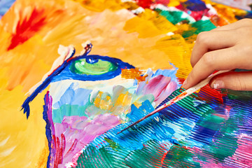 A girl paints a colorful lion on canvas using a brush and knife. Closeup, selective focus