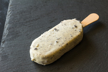 Ice cream lolly with white chocolate coating and dark chocolate cookie crumbs isolated on black background - side view