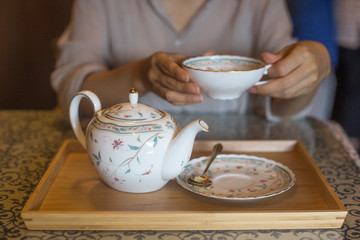 A woman pouring black tea from the ceramic teapot in cafe.