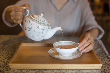 A woman pouring black tea from the ceramic teapot in cafe.