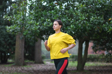 Sporty woman running at city park in autumn. Female athlete exercising outdoor.