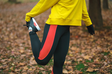Female athlete stretching at city park in autumn. Detail sporty woman legs exercising outdoor.