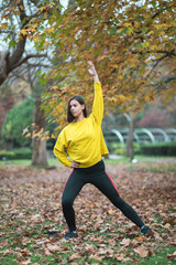 Female athlete stretching at city park in autumn. Sporty woman exercising outdoor.