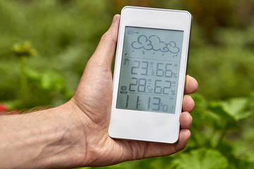Best personal weather station device with weather conditions inside and outside. A man holds a gadget in her hand on a background of green foliage.