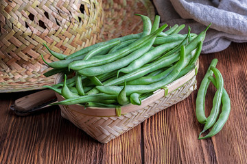 Fresh and raw green beans (green round beans) in wicker basket. Rustic and homemade look on wooden...