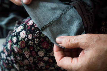 Macro elderly woman hands sewing on fabric, needle. Sew pants by old woman hand, seamstress at work with cloth fabric. Grandmother sews. Close up shot. Selective focus