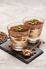 Portion of Classic tiramisu dessert in a glass cup on stone serving board on concrete background