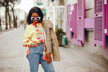 Obraz premium A beautiful and stylish black girl with long dark hair dressed in a brown coat and shirt wallking in a summer city