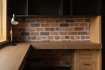 Modern corner workplace with lamp on empty wooden table with cabinets against brick wall