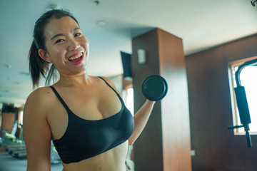 young pretty and happy Asian Chinese woman working hard at hotel gym or fitness center lifting dumbbell doing body building indoors workout in healthy lifestyle concept