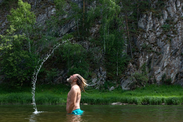 Model aged bearded man  splashing water with his hair. Hair whip. .against a green summer background