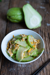 Fresh chayote fruits (Sechium edulis) stir fried with egg and garlic in bowl on wood background