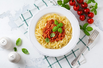 Traditional Italian dish fettuccine pasta with bolognese sauce, basil and parmesan cheese in a white plate on a light wooden background. Top view.