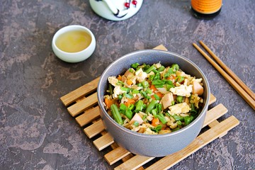 Fried rice with green green beans, carrots, egg and ham in a gray bowl on a dark brown concrete background. Selective focus. Asian food. Copy space.