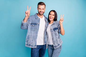 Portrait of cheerful married guy and girl making v-sign wearing denim jeans isolated over blue background