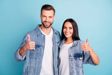 Portrait of charming spouses showing thumb up wearing denim jeans isolated over blue background