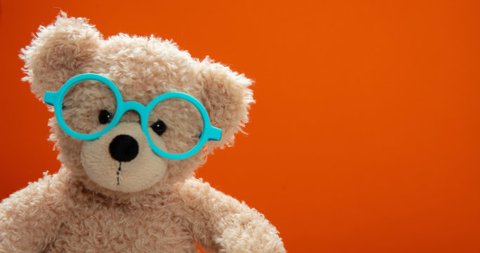 Cute teddy wearing eyeglasses against orange color background