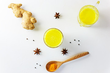 Golden milk from turmeric, vegetable milk, pepper, ginger, coconut oil, maple syrup in a glass on a white background. Traditional indian drink.