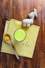 Golden milk from turmeric, vegetable milk, pepper, ginger, coconut oil, maple syrup in a glass on a wooden table. Traditional indian drink.