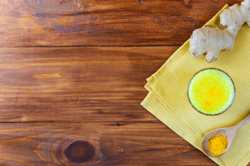 Golden milk from turmeric, vegetable milk, pepper, ginger, coconut oil, maple syrup in a glass on a wooden table. Traditional indian drink.