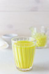 Golden milk from turmeric, vegetable milk, pepper, ginger, coconut oil, maple syrup in a glass on a white background. Traditional indian drink.