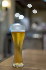 Cold beer in the glass on wooden table in cafe restaurant with bokeh light for vintage background concept, lifestyle design with copy space for text, advertising and banner.