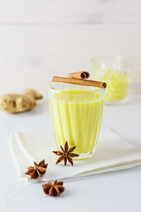 Golden milk from turmeric, vegetable milk, pepper, ginger, coconut oil, maple syrup in a glass on a white background. Traditional indian drink.