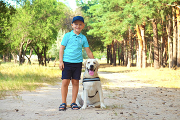 Portrait of cute blond boy hanging out with his pet friend labrador retriever out in the woods. Little guy standing six months old doggy, walk in a park. Background, copy space, close up.