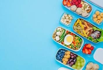 Plastic lunch boxes filled with healthy food on blue background with copy space