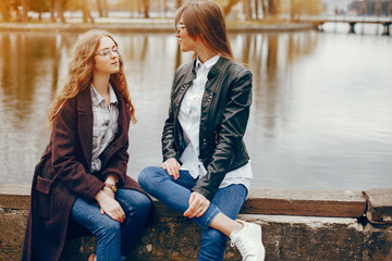 a beautiful stylish young girl with long curly hair and a long coat sitting in the autumn park near...