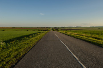 old asphalt road through green fields at sunset