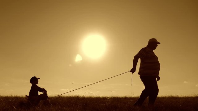 Senior man grandfather teaches his grandson to ride a bike in nature. He pulls it by the rope, the kid learns to ride a bicycle, fun for the family in the outdoor during sunset. Generation concept.