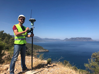 Geodetic engineer surveyor in white hard hat doing measurements with GNSS satellite receiver