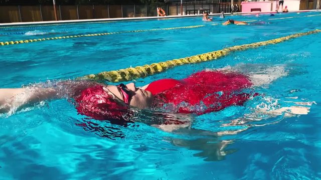 Girl swimming backstroke in slow motion. Professional swimmer practicing in olympic pool outdoor