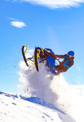snowmobile jump. bright snowmobile in motion. the guy is flying on a snowmobile on a background of blue sky leaving a trail of splashes of white snow. bright snowmobile and suit without brands. super