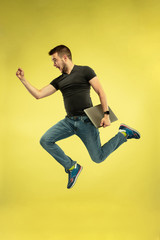 Fototapeta na wymiar Superman. Portrait of happy jumping man with gadgets isolated on yellow background. Modern technologies, freedom of choices concept, emotions concept. Using laptop and smartwatches in flight.