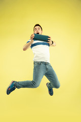Fototapeta na wymiar Sky sound. Full length portrait of happy jumping man with gadgets on yellow background. Modern tech, freedom of choices concept, emotions concept. Using portable speaker like superhero in flight.