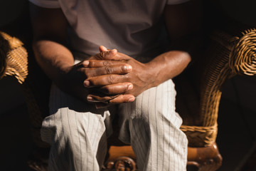 Senior man sitting on wicker chair with hands clasped at home 